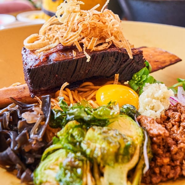 NōKA Ramen & Bar's ramen dish with a large piece of meat, egg yolk, and various toppings.