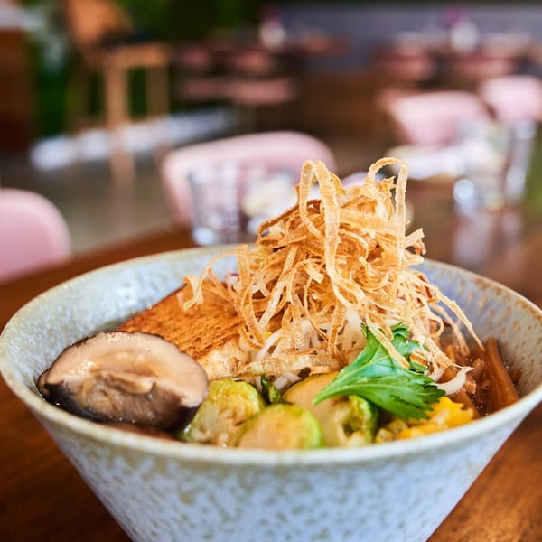 A bowl of NōKA Ramen with crispy fried onions, tofu, mushrooms, and brussels sprouts.