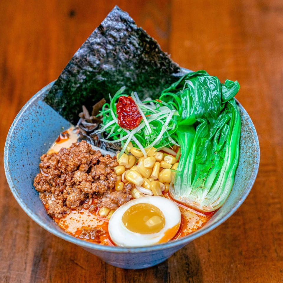 A vibrant bowl of NōKA Ramen with ground pork, corn, bok choy, nori, and a soft-boiled egg.