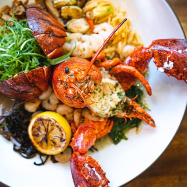 A large plate of NōKA Ramen's lobster and shrimp pasta with grilled lemon and greens.